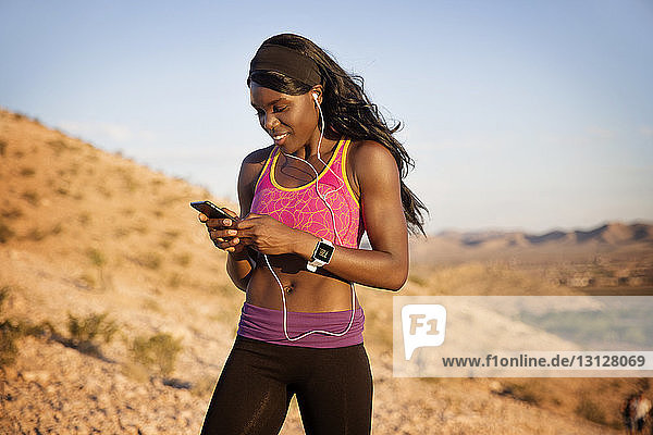 Smiling sportswoman listening music while exercising against hills