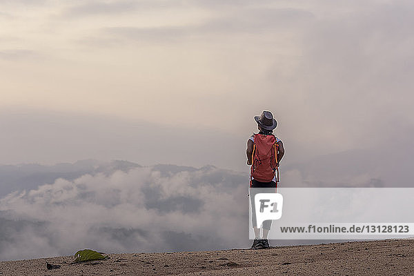 Rückansicht einer Wanderin mit Rucksack  die bei nebligem Wetter auf dem Berg steht