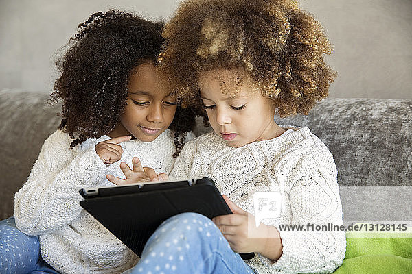Schwestern benutzen digitales Tablet  während sie zu Hause auf dem Sofa sitzen