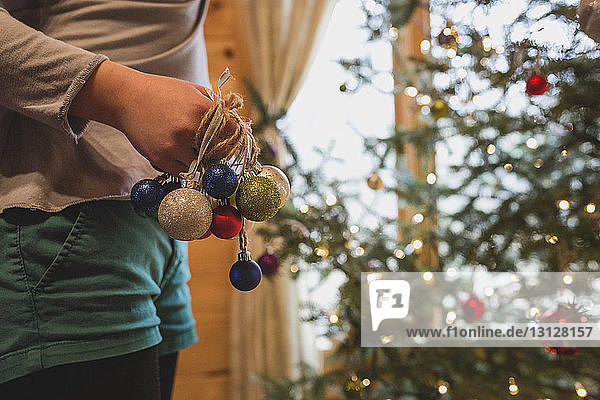 Midsection of girl with baubles decorating Christmas Tree at home