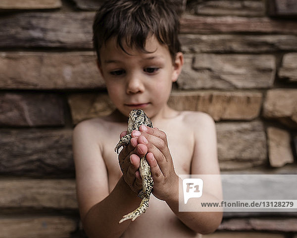Playful boy holding frog while standing against wall