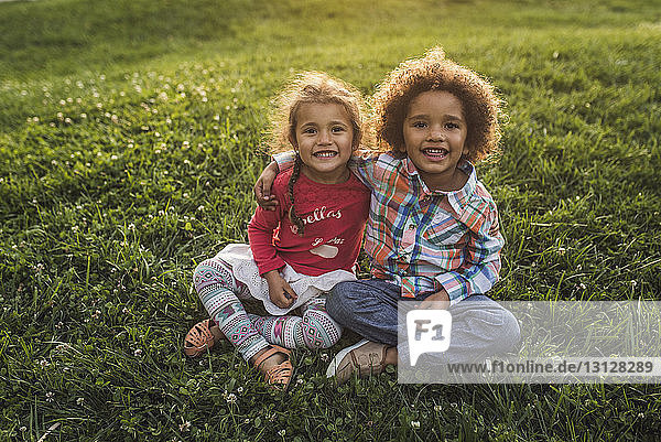 Portrait of smiling siblings sitting on grassy field at park