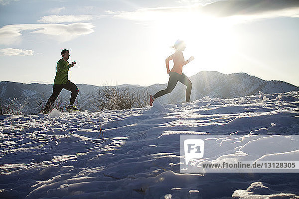 Niedrigwinkelansicht eines Paares  das auf einem Schneefeld gegen den Himmel joggt