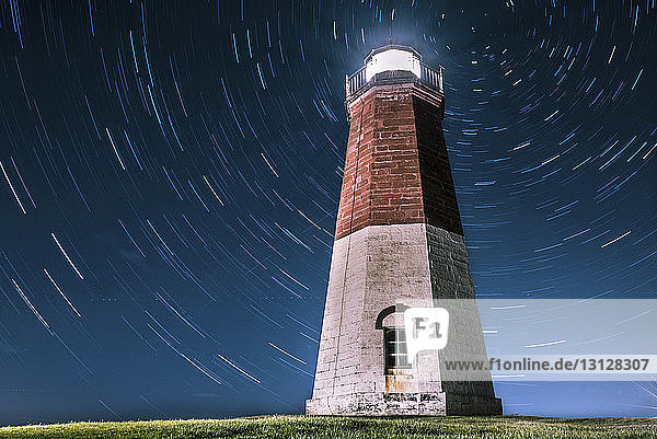 Low angle view of illuminated lighthouse against star trails at night