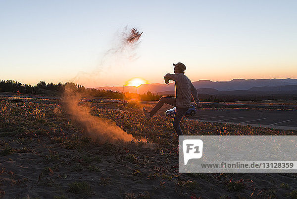 Seitenansicht eines glücklichen Mannes  der bei Sonnenuntergang auf dem Feld gegen den Himmel tanzt