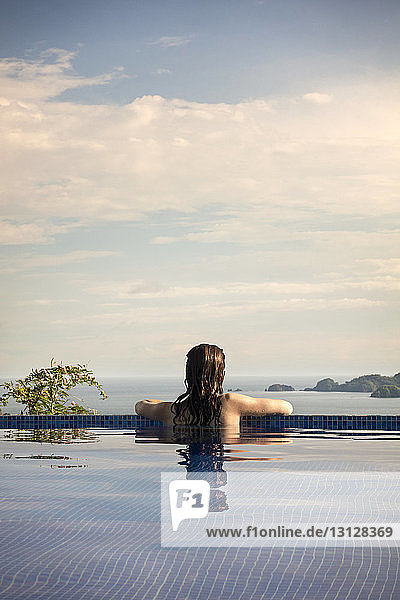 Rear view of woman in swimming pool enjoying view of Costa Rica against cloudy sky