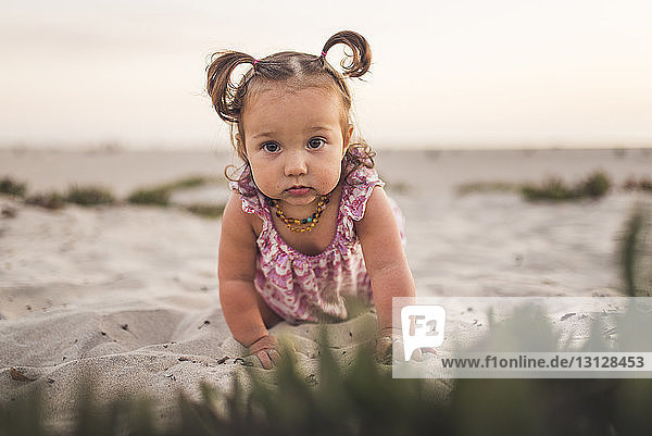 Portrait of cute baby girl crawling on sand at beach