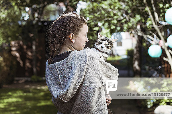 Rückansicht einer Frau  die eine Katze trägt  während sie im Hinterhof steht