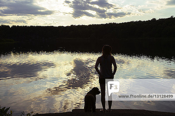 Rückansicht einer am See stehenden Frau mit Hund