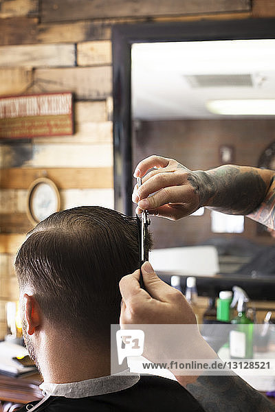 Ausgeschnittenes Bild von Händen  die einem Mann beim Friseur die Haare schneiden