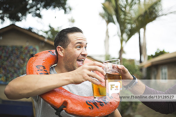 Beschnittenes Bild einer Hand  die mit einem glücklichen Freund auf ein Bierglas anstößt  während sie im Hinterhof steht