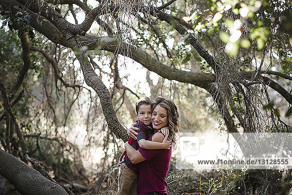 Portrait of son embracing smiling mother against branches at forest