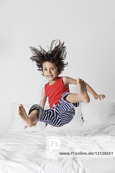 Porträt eines glücklichen Jungen  der zu Hause auf dem Bett gegen die Wand springt