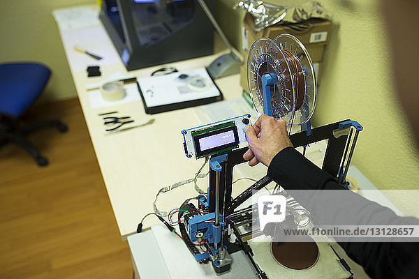 Abgehackte Hand eines Ingenieurs untersucht 3D-Drucker auf Tisch im Büro