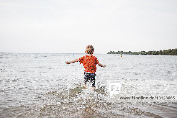 Rear view of playful boy running in sea against clear sky