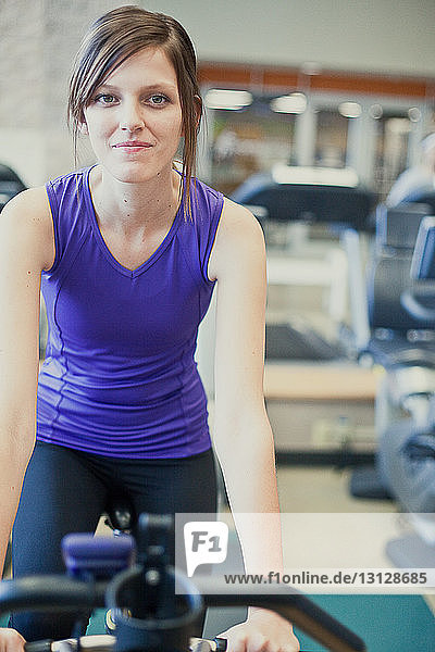 Porträt einer lächelnden Frau auf dem Heimtrainer im Fitnessstudio