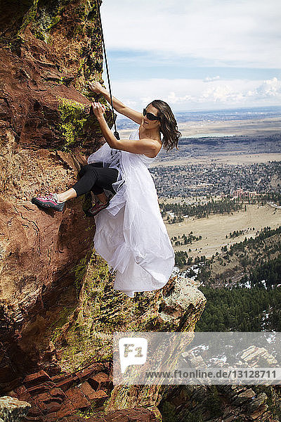 Woman in wedding dress climbing mountain against sky