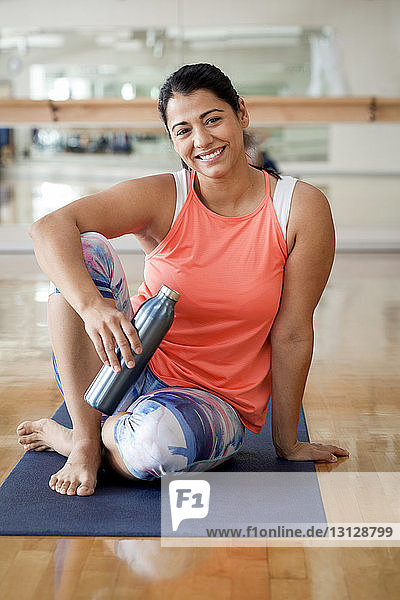 Porträt einer lächelnden Frau  die eine Flasche in der Hand hält  während sie im Fitnessstudio sitzt