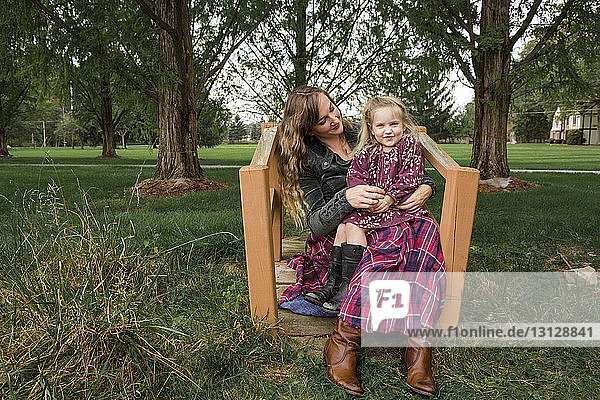 Porträt einer Tochter  die im Park auf dem Schoss der Mutter sitzt