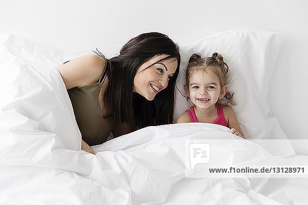Smiling mother and daughter sitting on bed at home