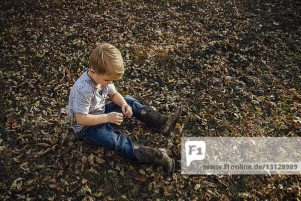 Hochwinkelaufnahme eines Jungen  der auf herabgefallenem Herbstlaub im Park sitzt