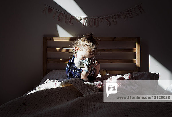 Mädchen umarmt Puppe  während sie zu Hause in der Dunkelkammer auf dem Bett sitzt