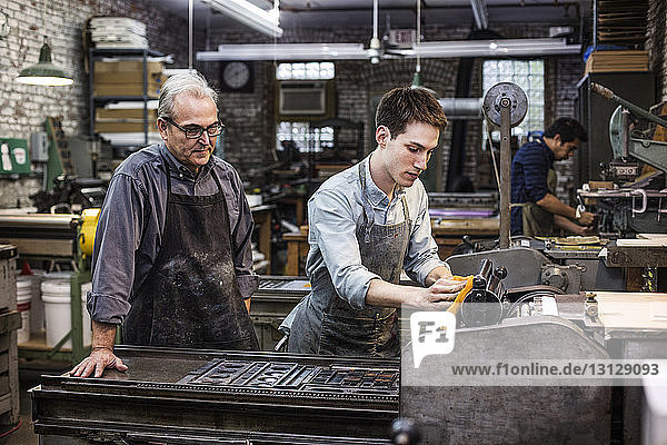 Leitender Mann betrachtet Mitarbeiter bei der Reinigung einer Druckmaschine in einem Workshop