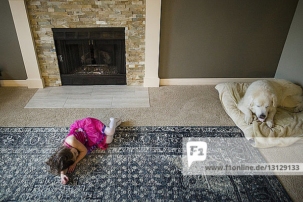 High angle view of girl lying by fireplace while dog relaxing on pet bed at home