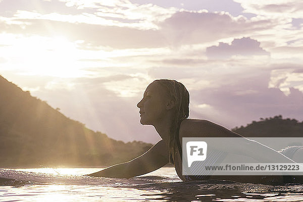 Seitenansicht einer Frau  die bei Sonnenuntergang auf einem Surfbrett im Meer liegt