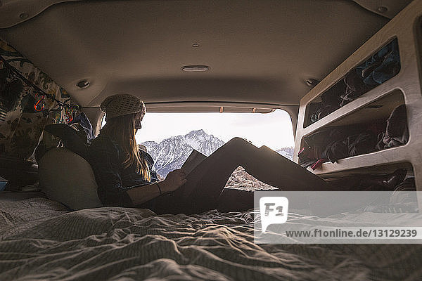 Frau liest Buch  während sie im Wohnwagen gegen die Berge sitzt