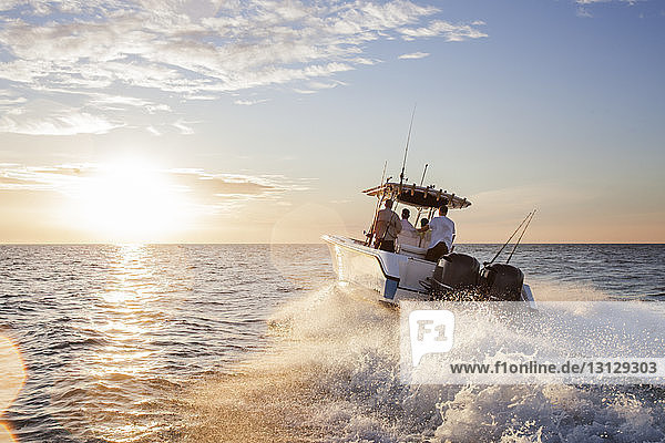 Männer genießen im Schnellboot auf See gegen den Himmel bei Sonnenuntergang