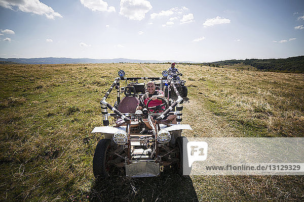 Friends riding off-road vehicle and quadbike on grassy field against sky