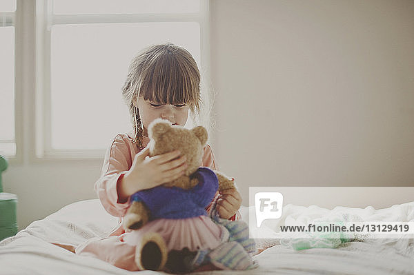Mädchen spielt mit Teddybär auf dem Bett