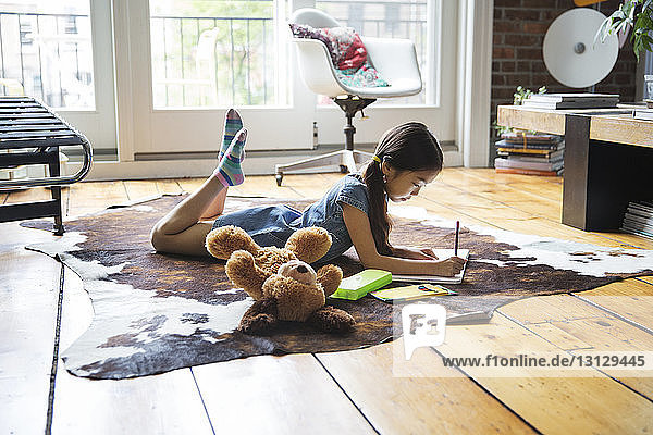 Mädchen liegt auf Teppich und schreibt zu Hause auf Buch