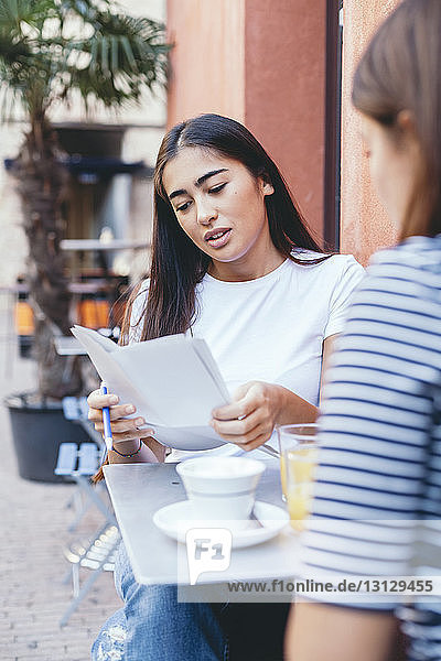 Frau liest Dokumente  während sie mit einem Freund an einem Tisch im Bürgersteig-Café sitzt
