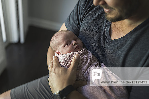 Midsection of father carrying newborn daughter at home