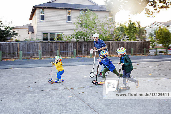 Father and sons enjoying with push scooter on street by houses