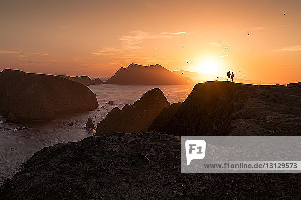 Silhouettenpaar steht auf Felsformation am Meer gegen den Himmel