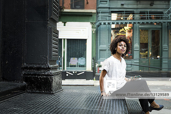 Porträt einer Frau  die ein Smartphone in der Hand hält  während sie auf einer Treppe in der Stadt sitzt