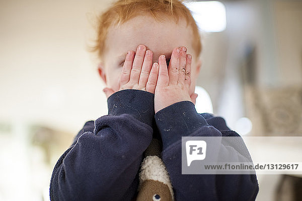 Cute baby boy hiding face while playing peekaboo at home