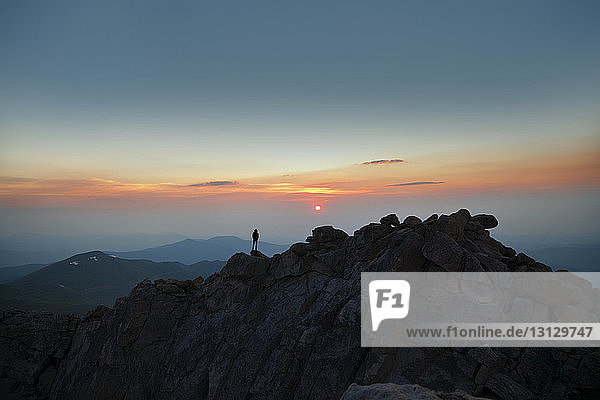 Fernansicht eines Mannes  der bei Sonnenuntergang auf einem Berg steht