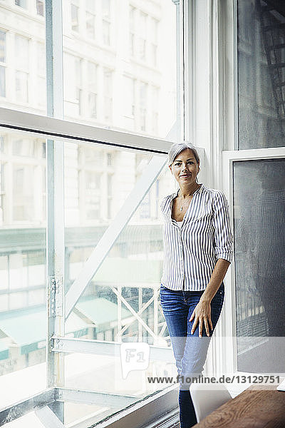 Porträt einer reifen Geschäftsfrau  die in einem kreativen Büro am Fenster steht
