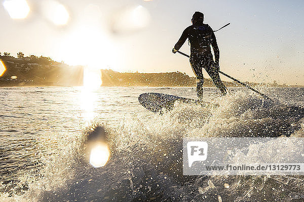 Rückansicht eines Mannes  der während des Surfens im Meer bei Sonnenuntergang die Stange hält