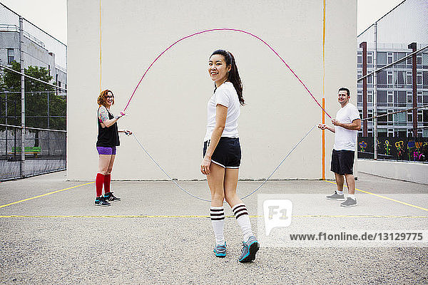 Portrait of woman walking towards friends swinging jump ropes on street against wall