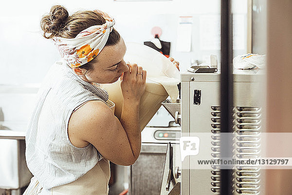 Frau gießt Zutaten in Eiscreme-Maschine in Großküche