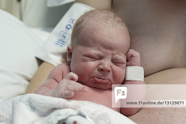 Close-up of newborn son crying by shirtless mother in hospital
