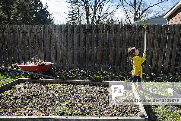 Mädchen  das im Herbst bei der Gartenarbeit im Garten mit dem Rechen spielt