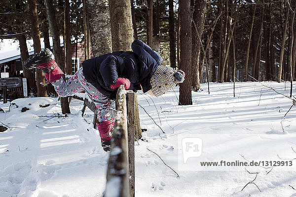 Side view of girl bending while standing on fence during winter