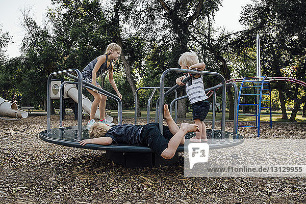 Siblings playing on carousel at playground