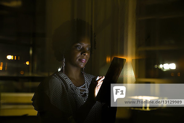 Geschäftsfrau mit Tablet-Computer in dunklem Büro durch Glas gesehen